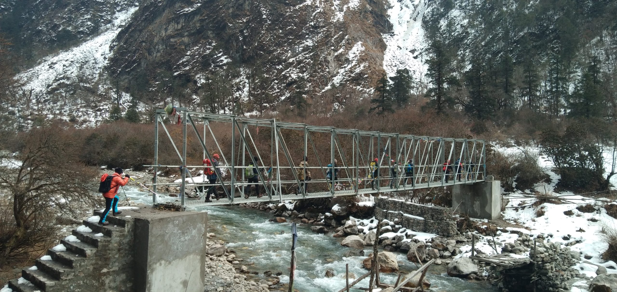 Suspension bridge over a river surrounded by mountains, captured during a Taktok Brothers trekking adventure.